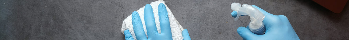 Hands in blue gloves cleaning a dark desk with a spray bottle and cloth